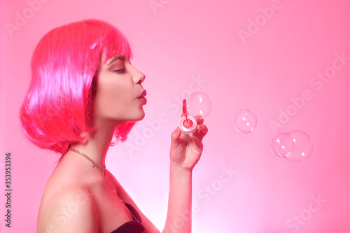 Girl with pink hair, brown hair. Model inflates a soap bubble, a woman on a pink background.