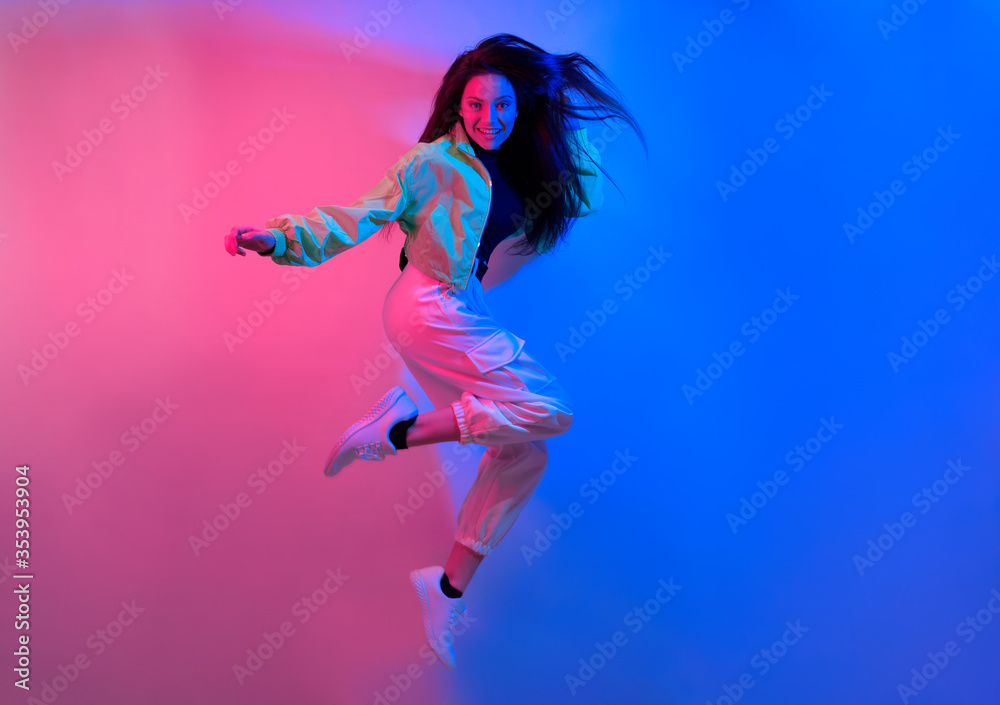 The brunette dances in neon, the dancer in red-blue. Hip hop girl, party, smile. Model in flight, jumping.