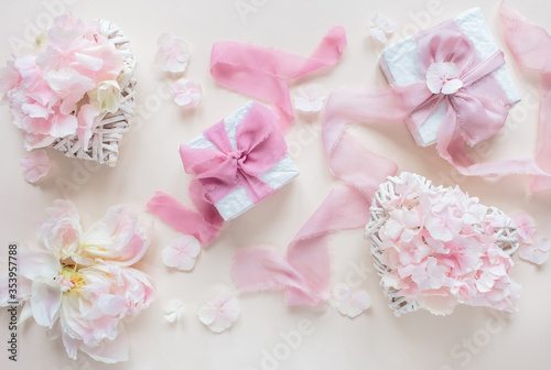 Top view composition of two gift boxes with silk pink ribbons and bows and two wicker hearts with pink flowers on a pastel beige background. Festive concept.
