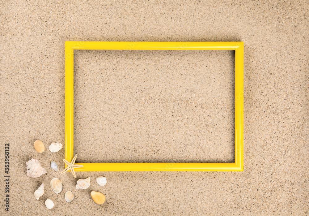 Fototapeta premium Yellow photo frame. Beach sand shells background.