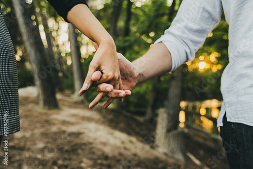 Close-up of the intertwined hands of a couple in love walking through a forest.
