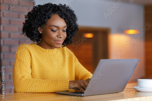 Young businesswoman typing email on laptop, sitting at cafe