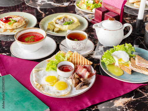 A set of several dishes for lunch  red soup borsch  sandwich  fried eggs  bacon  black tea  lunch in a restaurant or cafe 