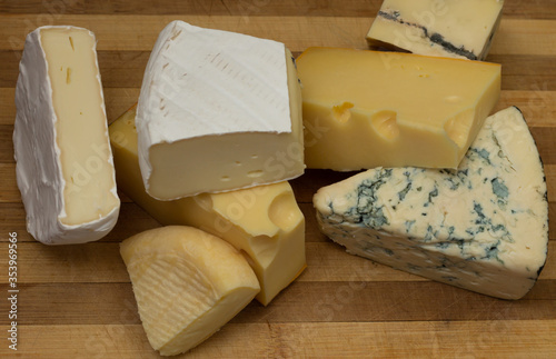 Different types of cheese on a rustic wooden cutting board. Top view.