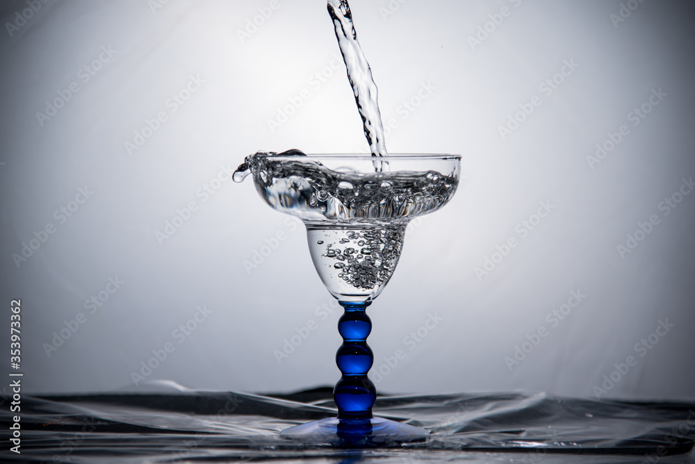 Clear liquid pouring into a margarita glass against a white background