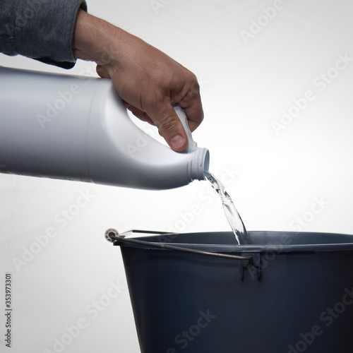 A man's hand pouring cleaner or bleach into a blue bucket against a white background. photo