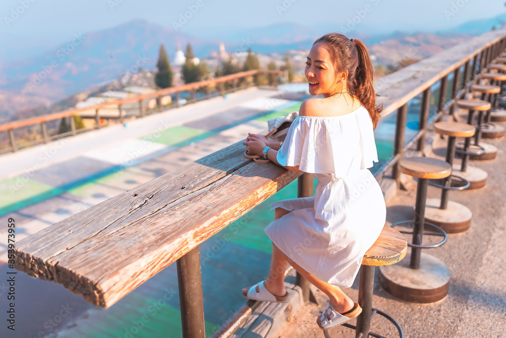 beautiful girl in white dress in holiday with sit on the chair wood in nature outdoor in sunset time by smile relaxing in vacation trip with blur background mountain at khao kho Thailand