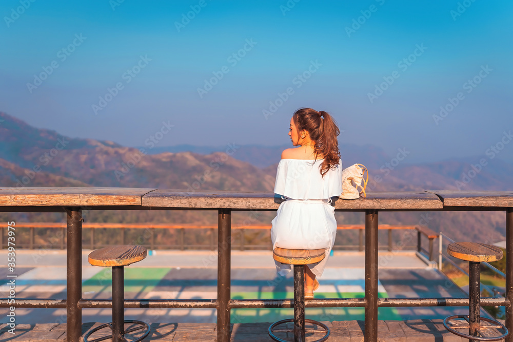 beautiful girl in white dress in holiday with sit on the chair wood in nature outdoor in sunset time by smile relaxing in vacation trip with blur background mountain at khao kho Thailand