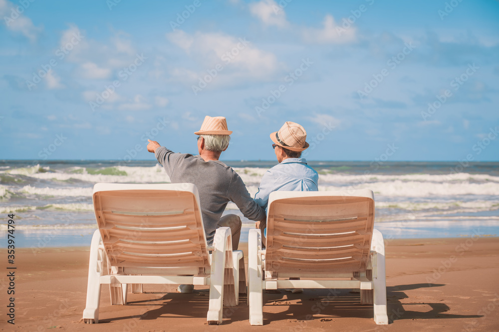 Rear view of senior couple sitting in deckchair on the beach together near sea and looking at the sea. Love is everything,.Retirement age concept and love, copy space for text