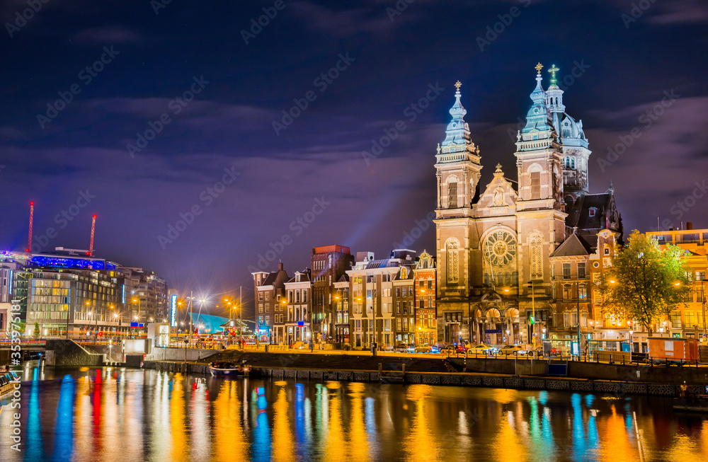 Night city view of Amsterdam canal and Basilica of Saint Nicholas, Holland, Netherlands.