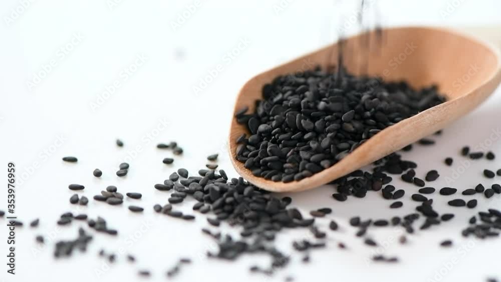 Sprinkling black sesame seeds on a wooden spoon, white background and slow motion Sprinkling black sesame seeds on a wooden spoon, white background and slow motion