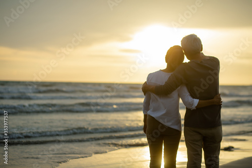 Rear view of Romantic senior embracing each other on the beach near the ocean at sunset..Retirement age concept and love, copy space for text
