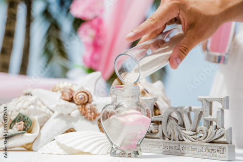 Bride and groom pouring colorful different colored sands into the crystal vase close up during symbolic nautical decor destination wedding marriage unity ceremony on sandy beach in front of the ocean 