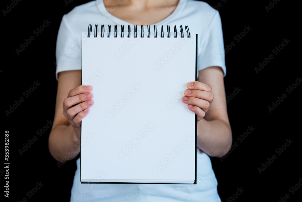 Torso of caucasian woman photographed against black background, holding up blank spiral bound note pad Torso of caucasian woman photographed against black background, holding up blank spiral bound note pad