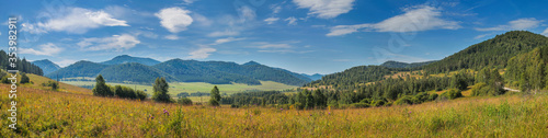 Panoramic view of a mountain valley. Meadow in the foreground, blue sky with clouds. Summer landscape.