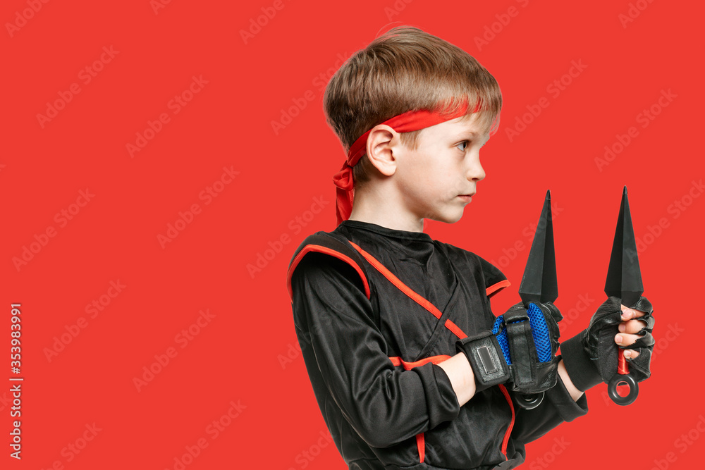 Portrait of young boy in kimono holding ninja kunai on red background Portrait of young boy in kimono holding ninja kunai on red background