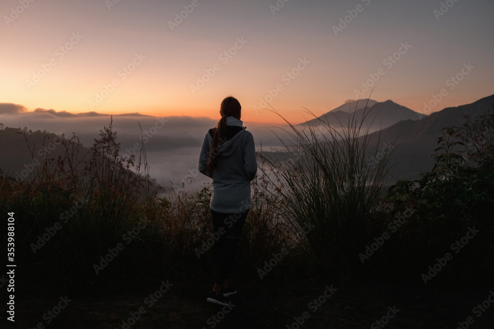 Cheering young woman hiker open arms to beautiful landscape on mountain peak. Girl hiker standing on the top of a mountain watching a beautiful scenery