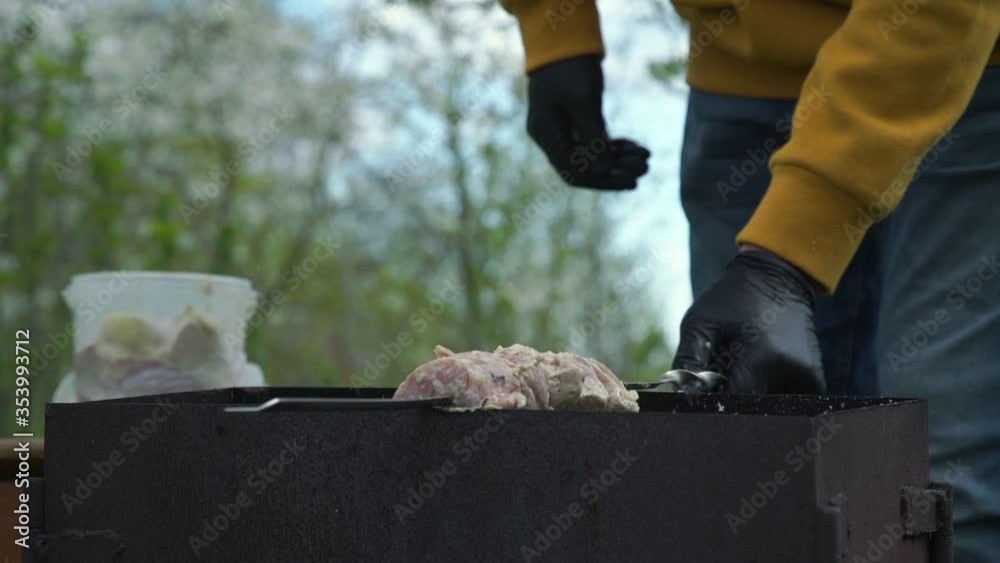 person in sterile gloves puts metal skewer with raw meat slices on black grill standing in garden slow motion close view person in sterile gloves puts metal skewer with raw meat slices on black grill standing in garden slow motion close view