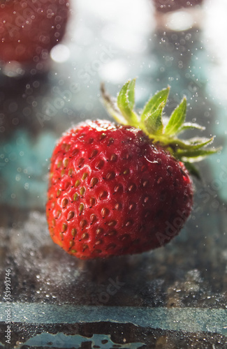 Some ripe fresh home grown strawberry on the light glass background with freeze spraying water drips. Back light. Copy space for text. Close up macro shoot.