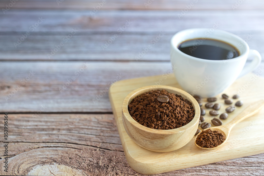 Ground coffee powder in a wooden cup and in a wooden spoon with a white coffee cup and coffee beans all on a wooden tray. Ground coffee powder in a wooden cup and in a wooden spoon with a white coffee cup and coffee beans all on a wooden tray.
