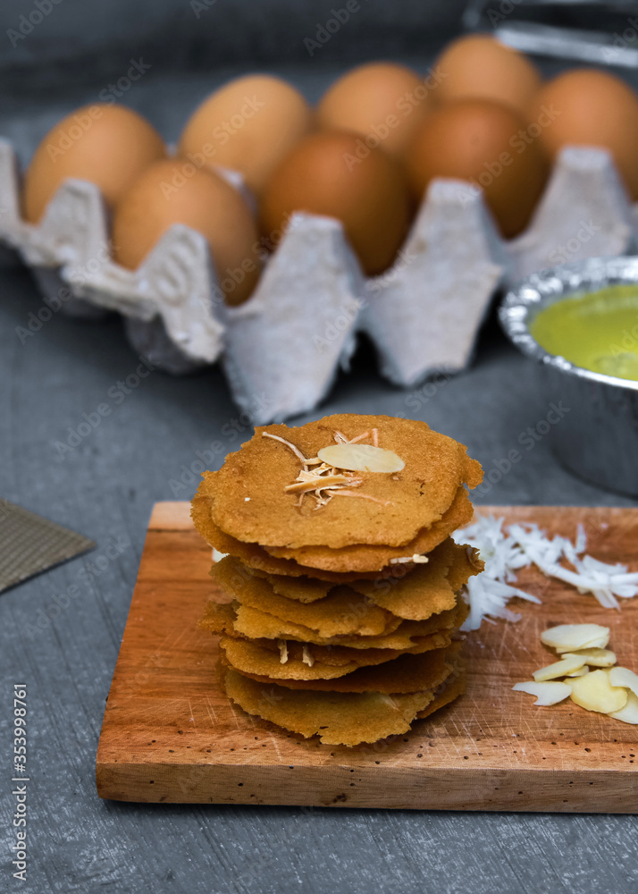 Almond crispy cheese on wooden board surounded by the ingredients such as eggs, cheese, chopped almonds, grated cheese, egg white and mixer. Food photography of thin crispy cookies