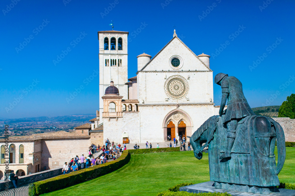 La Basilica di San Francesco ad Assisi, Umbria, Italia, con il prato antistante e il cielo blu sullo sfondo