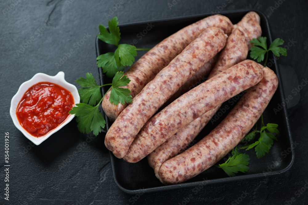 Cast-iron tray with raw fresh pork and poultry sausages, horizontal shot on a black stone background Cast-iron tray with raw fresh pork and poultry sausages, horizontal shot on a black stone background