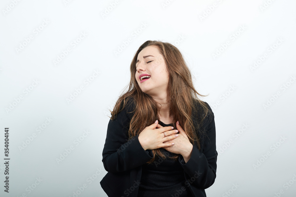 Young Attractive Woman Brunette In In A Black T-Shirt, Sweater On White Background, Cute Female Puts Hands On Her Chest, Smiles. The Concept Tenderness And Mercy Of People Young Attractive Woman Brunette In In A Black T-Shirt, Sweater On White Background, Cute Female Puts Hands On Her Chest, Smiles. The Concept Tenderness And Mercy Of People
