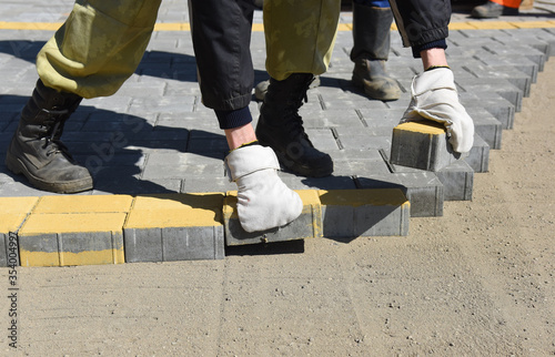 A worker puts paving slabs in straight rows, builds a pedestrian road.