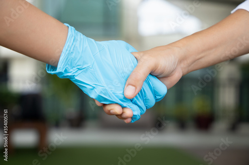 new normal hand shake between people following social distancing or personal distancing guideline by using clean new rubber glove to avoid direct contact while hand shaking with other people
