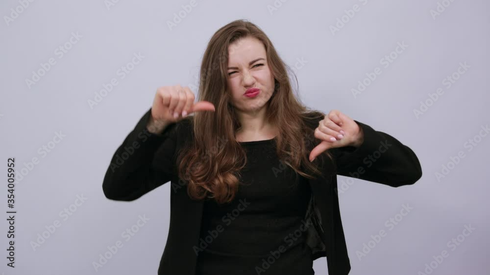 Young Attractive Woman Brunette In In A Black T-Shirt, Sweater On White Background, Dissatisfied Female Returned Thumb Finger To Bottom And Demonstrates Disagreement. Opposition, People's Protest Young Attractive Woman Brunette In In A Black T-Shirt, Sweater On White Background, Dissatisfied Female Returned Thumb Finger To Bottom And Demonstrates Disagreement. Opposition, People's Protest