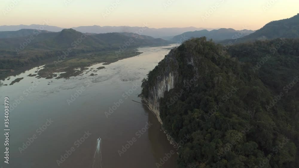 Aerial shot of speedboat on river against sky during sunset, drone flying forward over beautiful mountains - Mekong River, Laos Aerial shot of speedboat on river against sky during sunset, drone flying forward over beautiful mountains - Mekong River, Laos