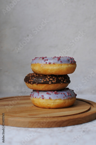 
multi-colored and chocolate donuts with sprinkles on a wooden board and grey background. Breakfast. Sweets, pastries. Colorful sweet glazed donuts from bakery. Food photo. Space for text