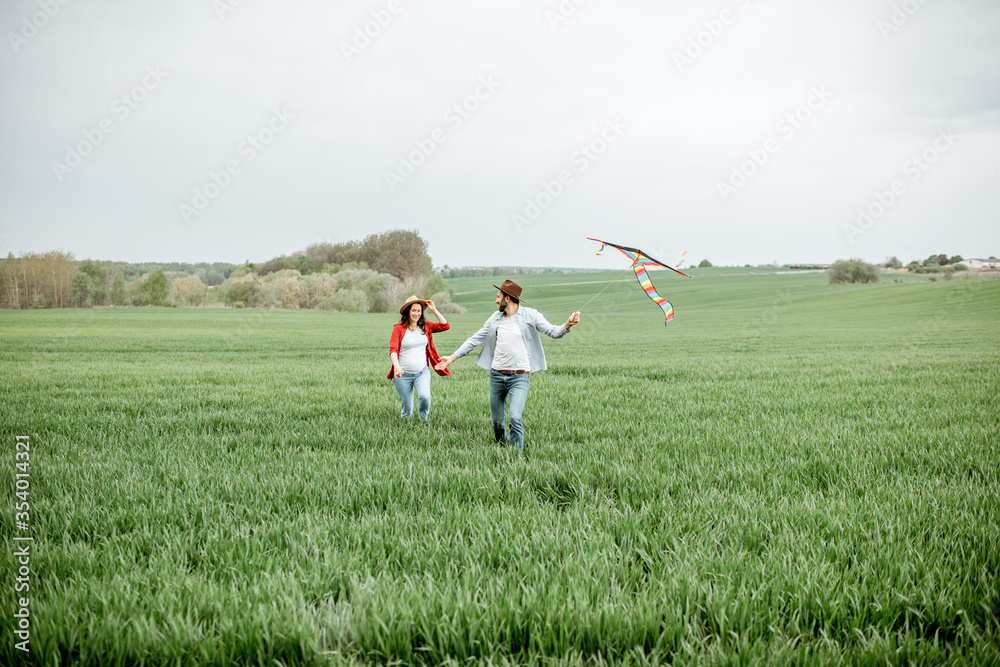 Happy couple having fun together, playing with kite on the greenfield. Happy couple expecting a baby and young family concept Happy couple having fun together, playing with kite on the greenfield. Happy couple expecting a baby and young family concept