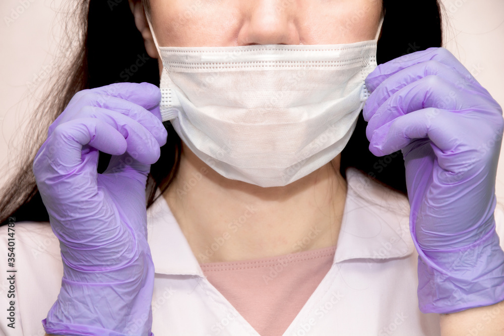 Fototapeta premium A young woman in lilac medical gloves puts a protective mask on her face . A confident girl, a female doctor in a medical mask.Protection AGAINST covid-19 coronavirus