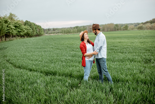 Portrait of a pregnant woman with her boyfriend dressed casually with hats standing together on the greenfield. Happy couple expecting a baby, young family concept