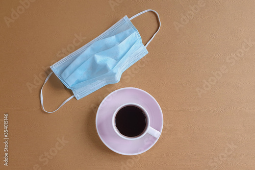 top view of a coffee cup and removed medical surgical mask on a brown table. Concept of protection. Minimal concept of health and allergies.  space for a text.  photo