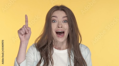 Close-up portrait of young woman showing idea gesture. Yellow background.