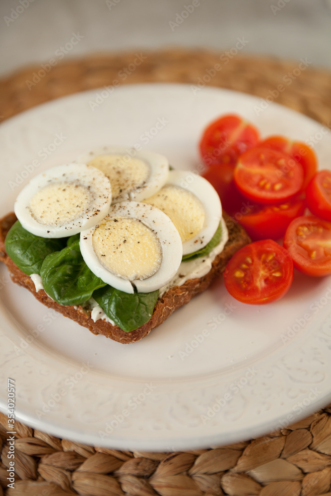 A white dish with egg sandwich, served with spinach and organic cherry tomatoes. Healthy snack or breakfast.