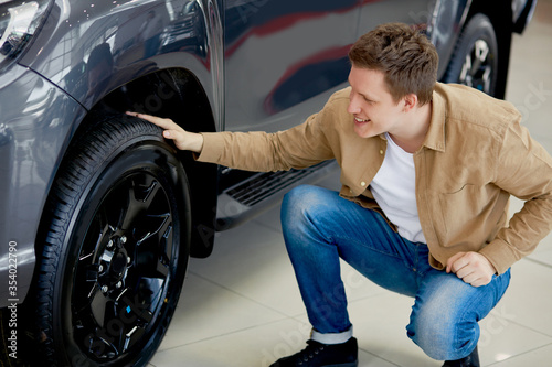 young caucasian man admires design of his new car in dealership, happy male enjoy perfectness of auto wheels © Roman