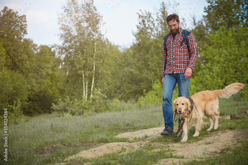 A bearded man in a red shirt with a Golden Retriever. The concept of travel in the open air.