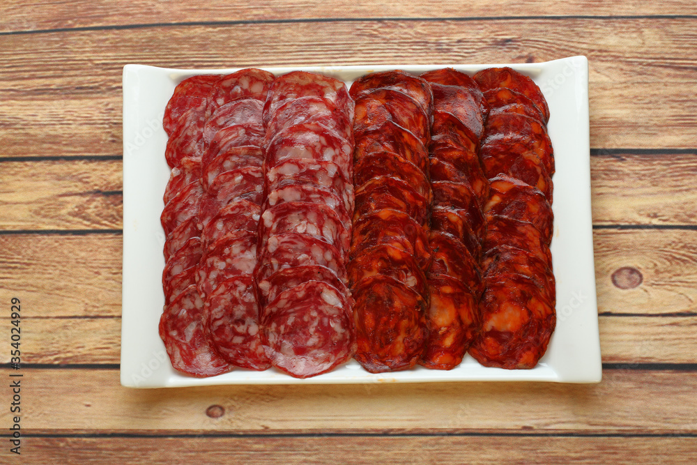 Combination ration of chorizo and acorn-fed Iberian sausage in white rectangular plate on wooden table seen from above Combination ration of chorizo and acorn-fed Iberian sausage in white rectangular plate on wooden table seen from above