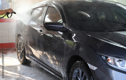 Closeup of grey car cleaning  washing with high pressure water spraying by male worker s hand. 