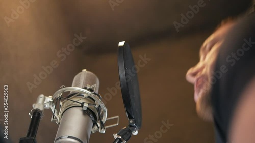 Male singer in headphones sings a song into the microphone at a recording studio. A young man emotionally writes a new song. Show Business