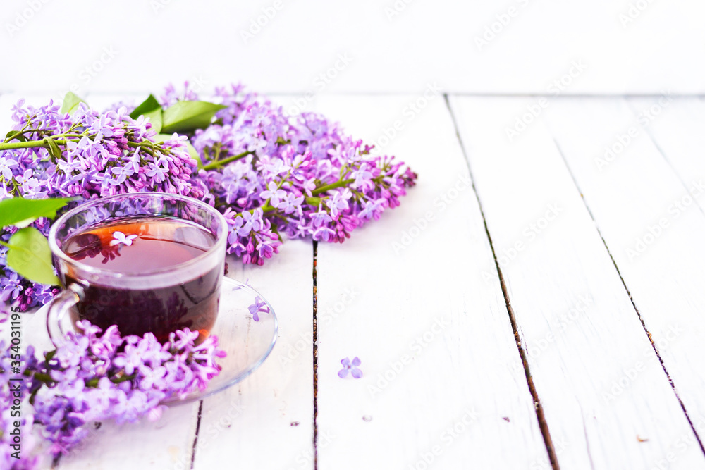 Cup of tea with lilac flowers on a wooden white background. Mocap for postcards. Spring time. Vase with lilacs. Copy space for text. The concept of holidays and good morning wishes