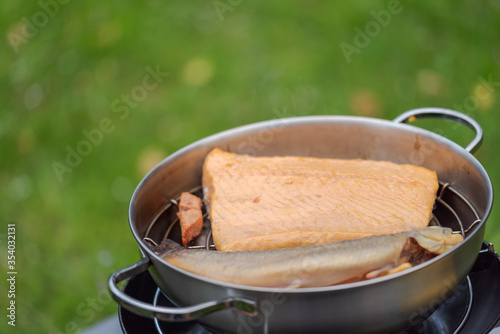 Big piece of salmon and one whole samlet lying in smoking pot with opened lid after preparation in outdoor kitchen with green grass background photo