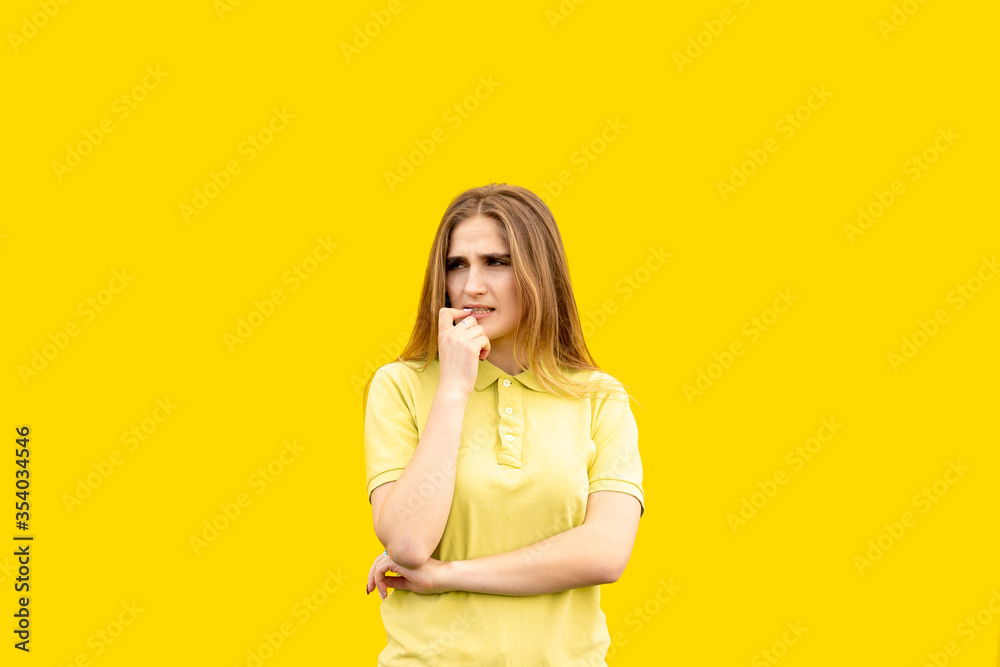A young girl bites her nails. Can't handle the problem. Can't relax. Dressed in a yellow T-shirt. Isolated on yellow background. A young girl bites her nails. Can't handle the problem. Can't relax. Dressed in a yellow T-shirt. Isolated on yellow background.