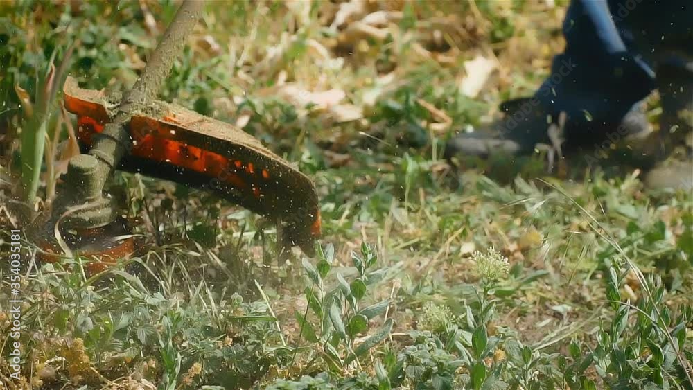 Professional gardener mowing lawn at home with electric brush cutter in slow motion and chunks of grass are flying around. Care of yard and household Professional gardener mowing lawn at home with electric brush cutter in slow motion and chunks of grass are flying around. Care of yard and household