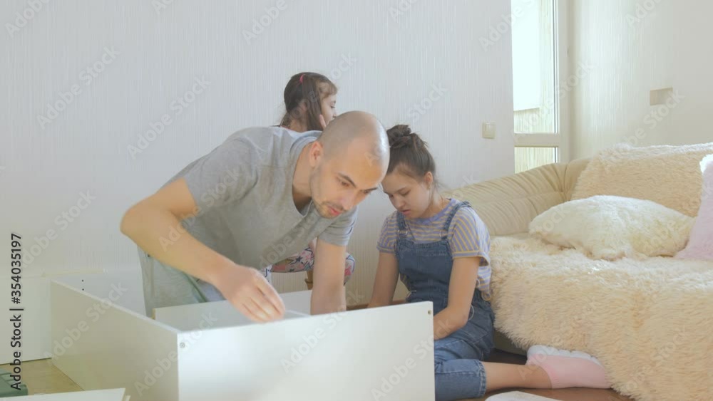 Two teenage sisters help their father put together a new shelves for the children's room. Two teenage sisters help their father put together a new shelves for the children's room.