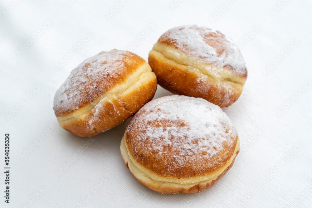 three donuts sprinkled with icing sugar on a light surface